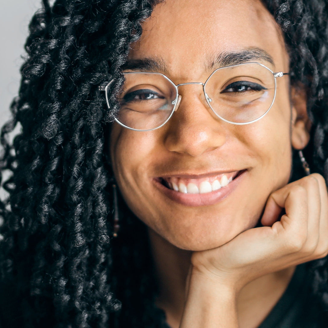 Woman with glasses smiling with hand on chin against a gray background