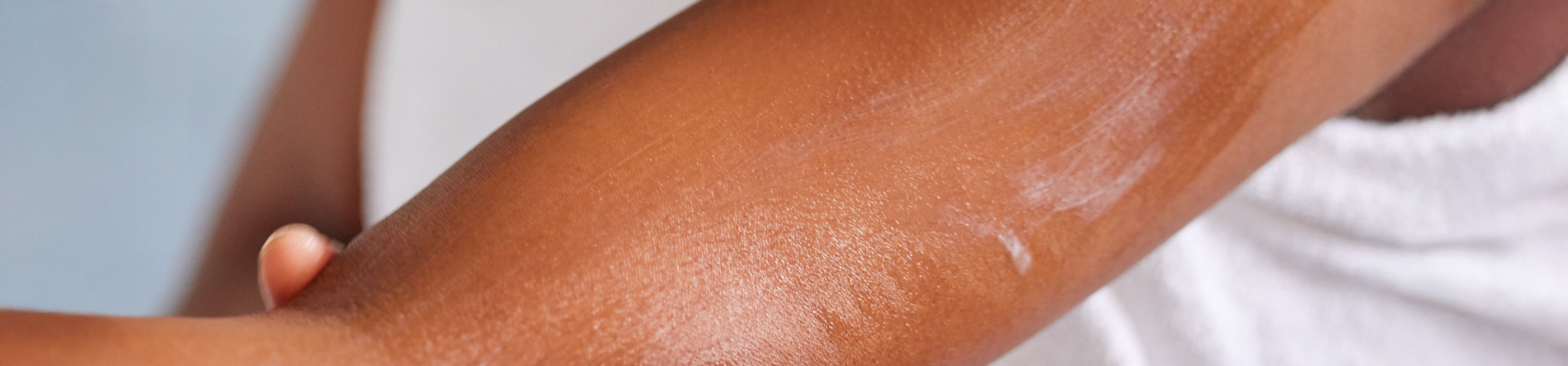Close-up of a person's forearm with a white cream or lotion applied, against a soft light blue and white background.