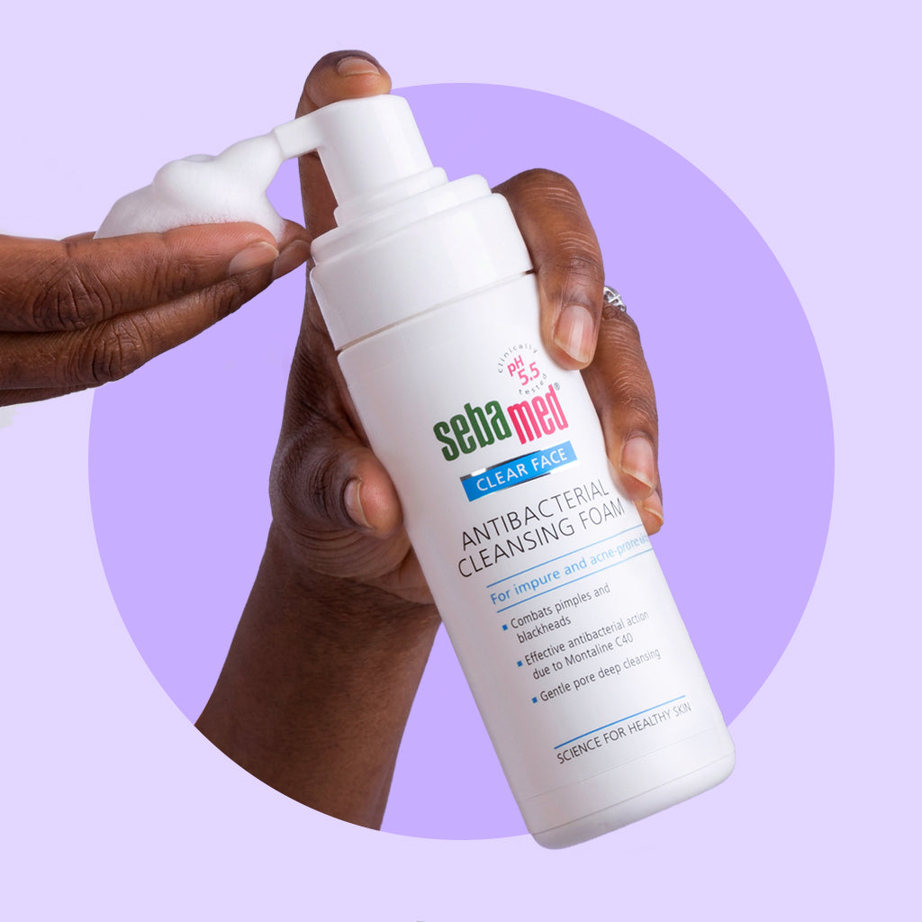 Hand holding a bottle of Sebamed antibacterial cleansing foam against a purple background